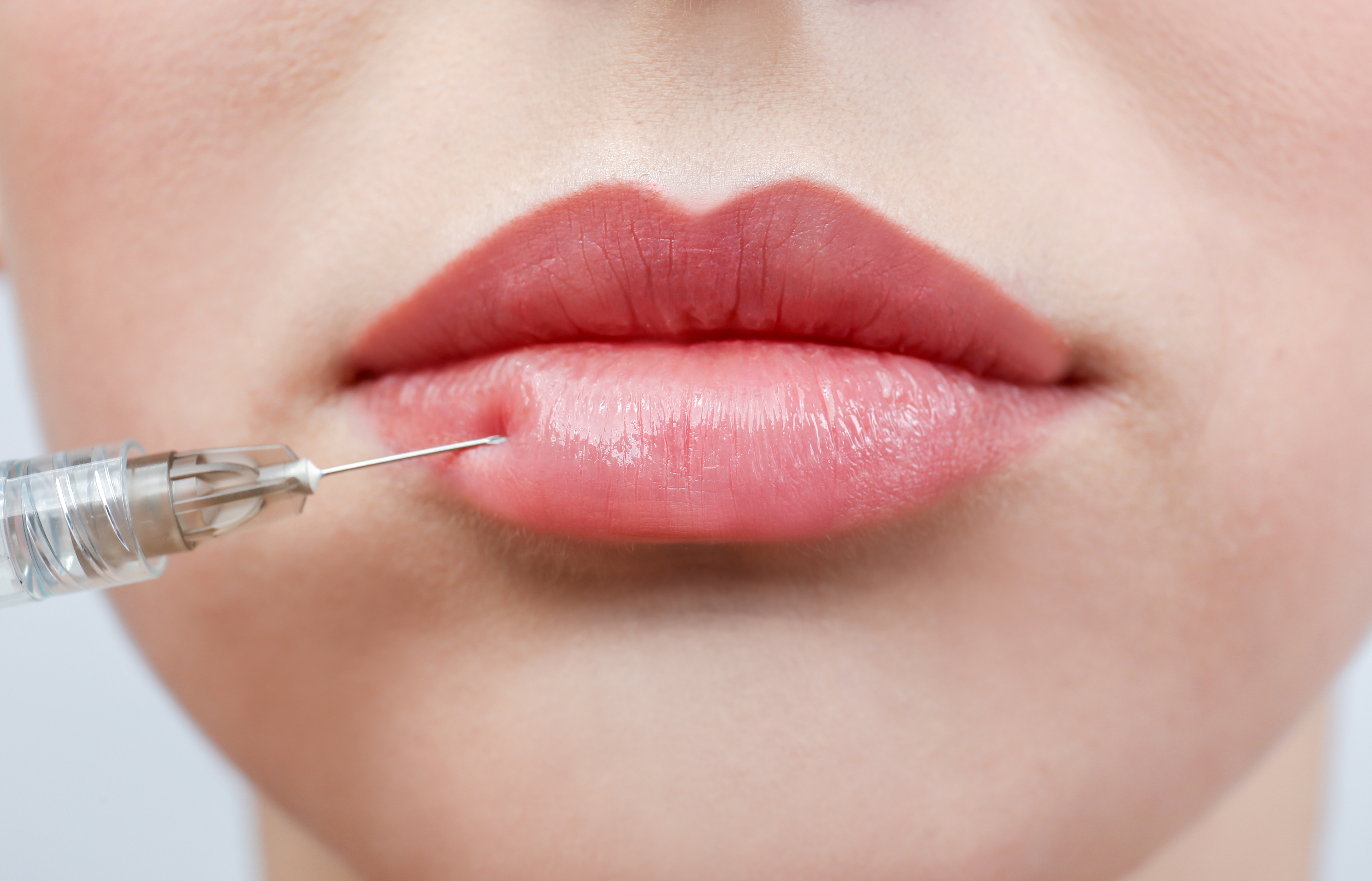 Beautiful young woman receiving filler injection in lips, closeup